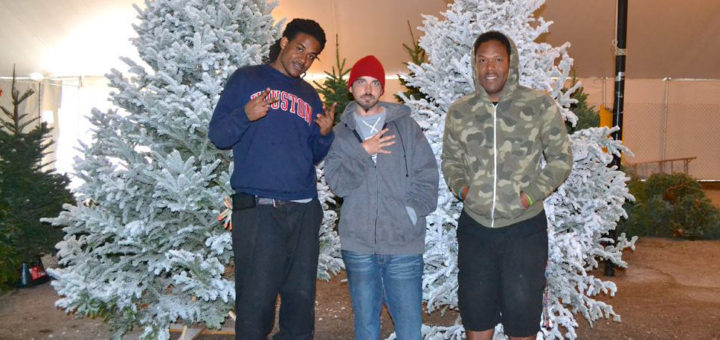 Three guys stand next to Christmas trees